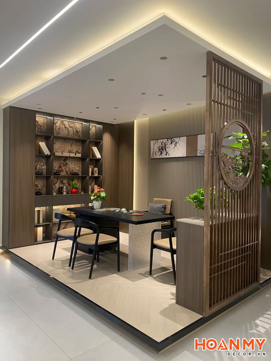 Phòng trà hiện đại với vách ngăn gỗ chữ nhật hoa văn tròn tinh xảo, bàn đen bóng, ghế đơn giản. Kệ gỗ tối led vàng, tranh trúc treo tường, cây xanh tươi mát.