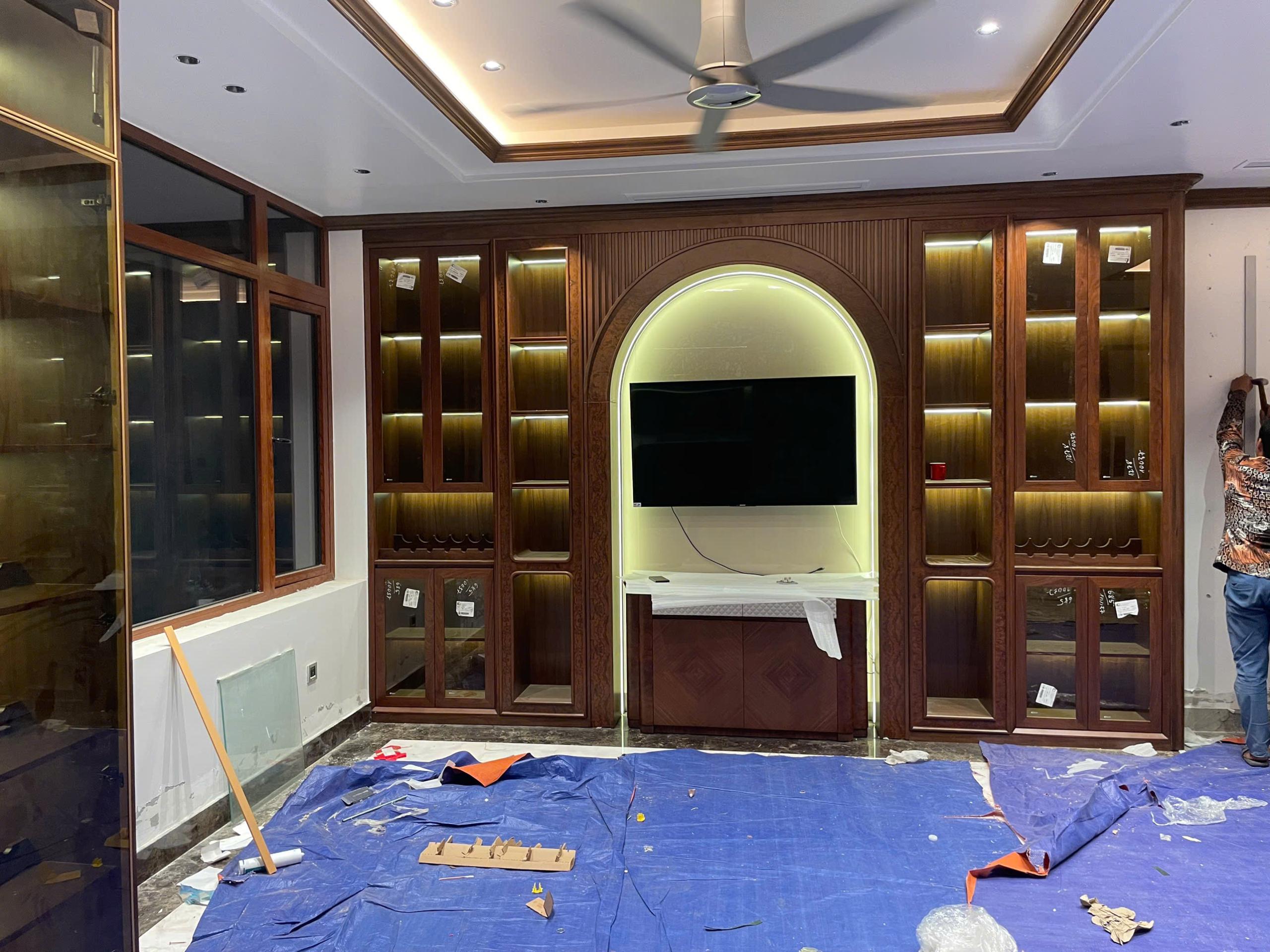 Hệ tủ trưng bày vân gỗ kết hợp ô TV dạng vòm và đèn hắt, sàn còn phủ bạt thi công.