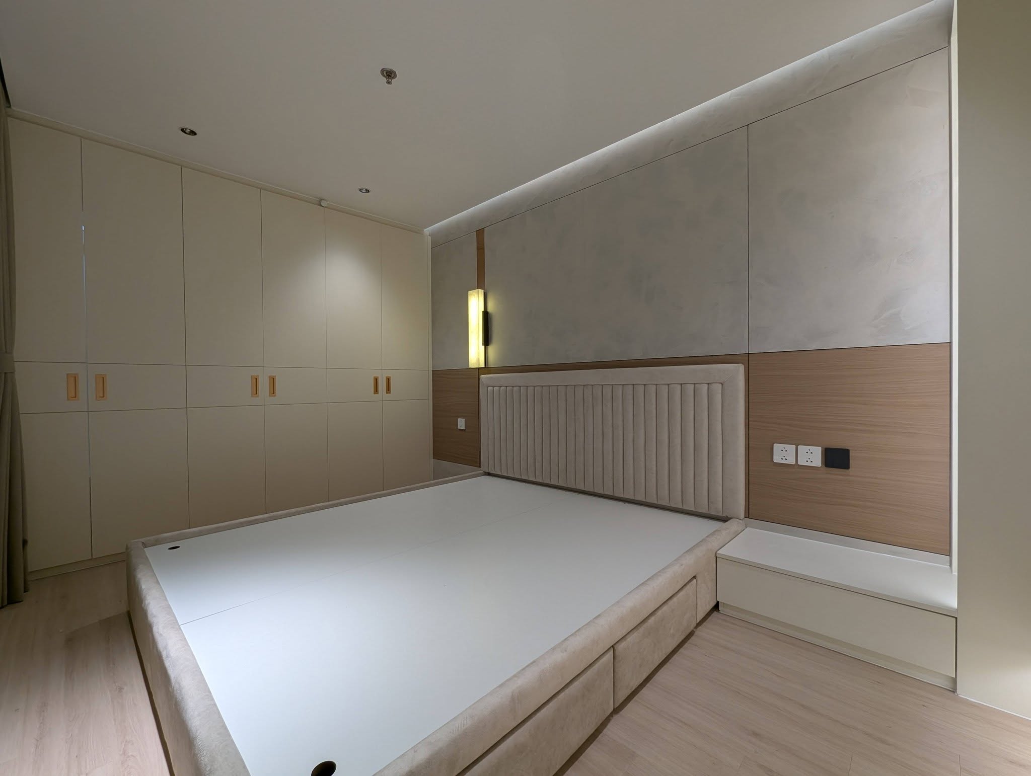 Phòng ngủ tông kem với giường, tủ áo kịch trần, vách đầu giường và tab gắn tường.