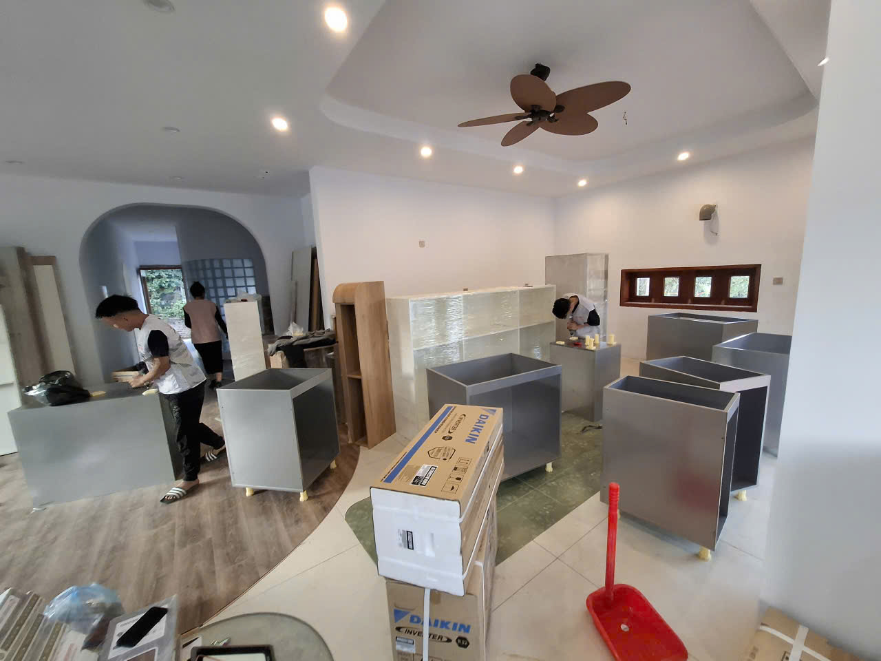 Thợ lắp ráp các thùng tủ rời trong phòng, xung quanh còn cấu kiện bọc màng và hộp vật tư.