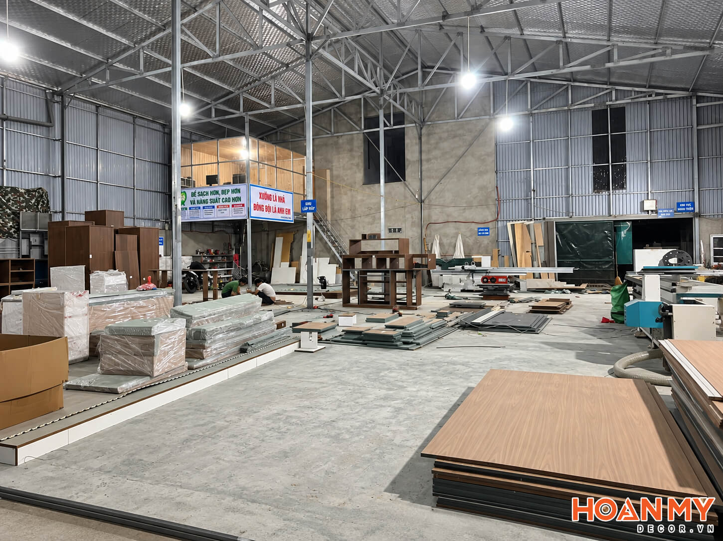 Lối đi trong xưởng giữa các chồng ván và cấu kiện nội thất đã bọc màng bảo vệ.