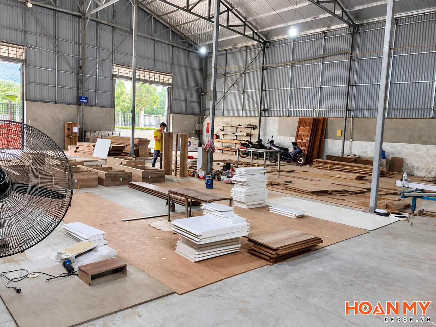 Các tấm ván trắng và vân gỗ được xếp theo chồng bên khu vực thợ đang gia công.