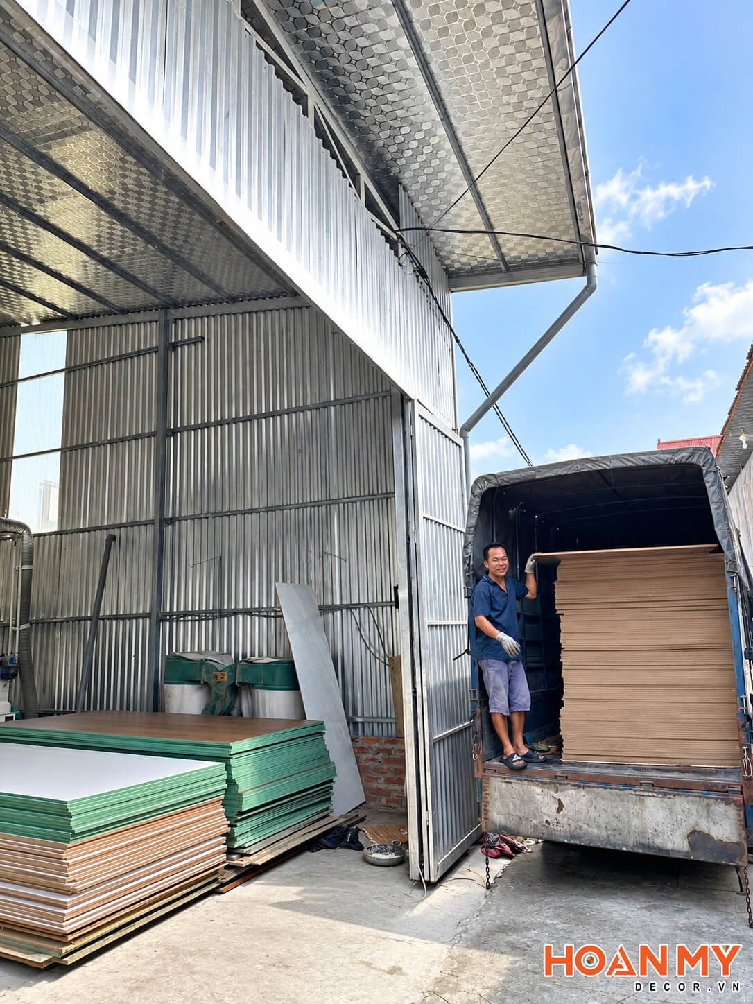 Xe tải đỗ sát cửa xưởng, bên trong thùng xe là các tấm ván được xếp chồng.