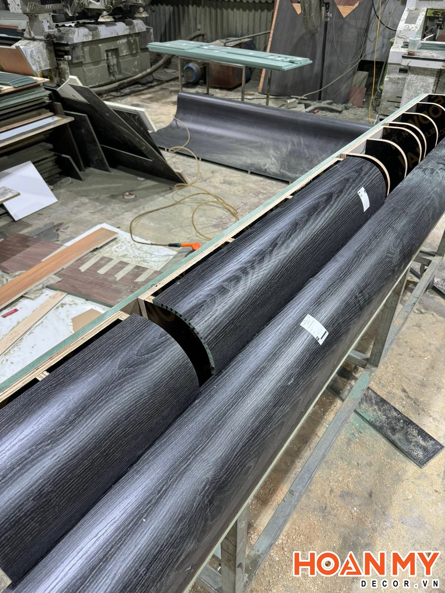 Các chi tiết cột bo tròn phủ vân sồi đen được định hình trên khung gá tại xưởng, chờ ghép vào hệ tủ.